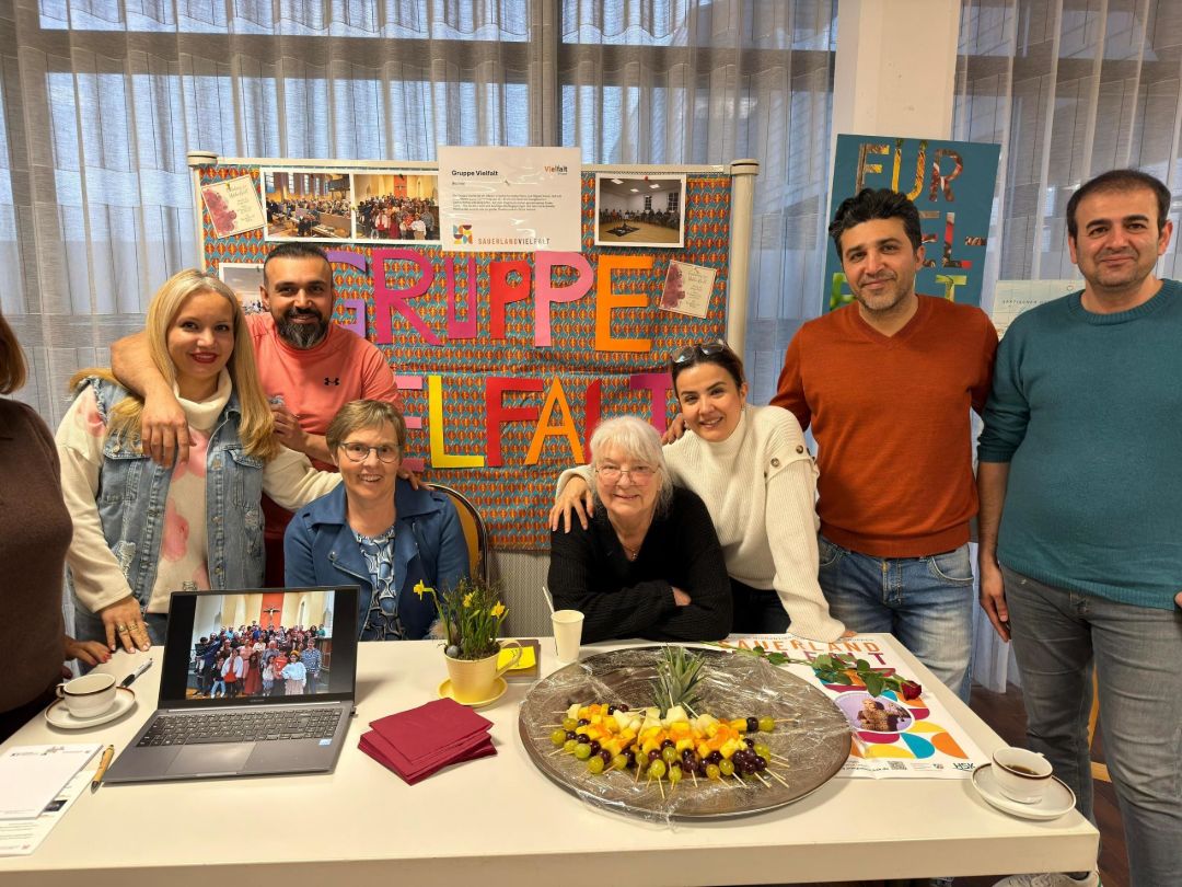 7 Personen werden vor einer Tafel  mit Informationen gezeigt. Sie nennen sich Gruppe Vielfalt.