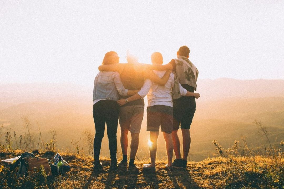 Vier Personen haben die Arme um ihre Schultern gelegt und schauen in den Sonnenuntergang