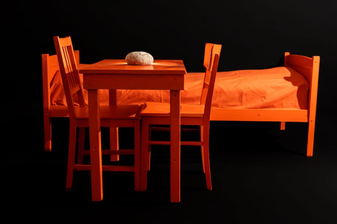 Ein Bett, ein Tisch, zwei St&uuml;hle. Alle in der Farbe orange.